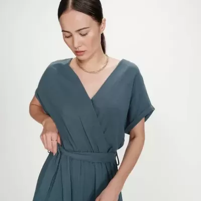 Vestido azul-acinzentado com decote em V e cinto, usado por mulher com colar dourado e anéis prateados.
