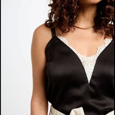 Top preto acetinado com rendas brancas por baixo e calças bege com risca de giz e cinto de laço