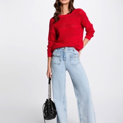 Mulher com suéter vermelho, jeans claros largos e bolsa preta com alça de corrente.