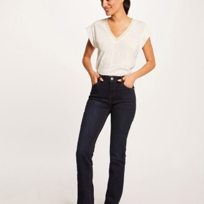 Mulher com calças de ganga azul escuro e camisola branca, a sorrir em fundo neutro