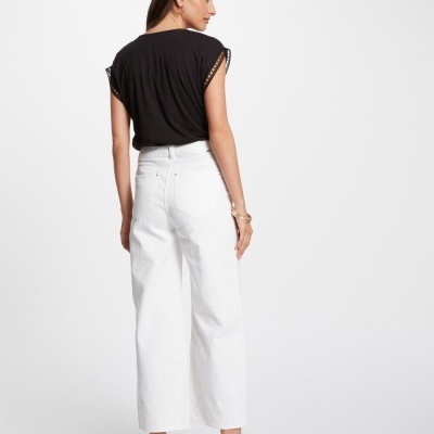 Mulher com calças brancas largas e top preto em fundo branco