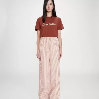 Modelo a usar t-shirt castanha com texto branco e calças largas às riscas vermelhas e brancas