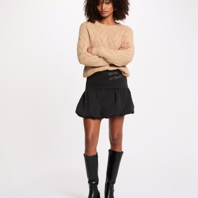 Mulher com camisola bege, saia preta e botas pretas