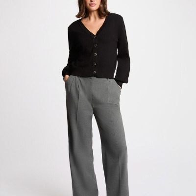 Mulher com cardigã preto e calças cinzentas num fundo branco