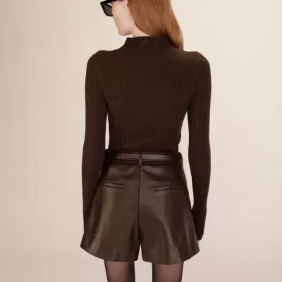 Pessoa vista de costas com camisola castanha e calções de pele castanha, em fundo claro