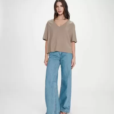 Mulher com blusa castanha de manga curta e calças de ganga largas azuis