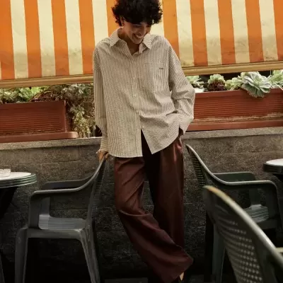 Pessoa com roupa casual numa esplanada com cadeiras de plástico e toldo às riscas laranja e bege