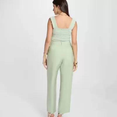 Mulher de costas com top e calças verdes em fundo branco