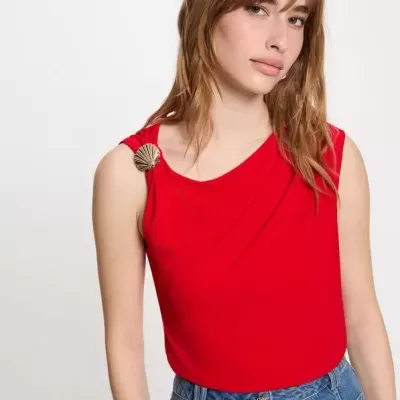Blusa vermelha sem mangas com joaninha dourada no ombro e calças de ganga azul