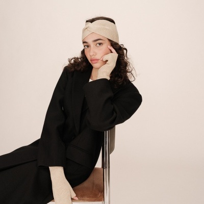 Mulher com casaco preto e acessórios bege de malha sentada numa cadeira