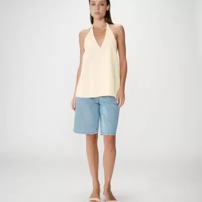 Mulher com top amarelo e calções de ganga azuis em fundo cinza