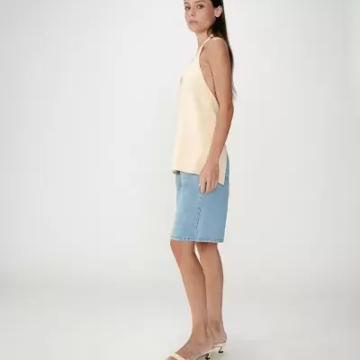 Mulher com top amarelo claro, saia jeans azul clara e sandálias amarelas de salto baixo, estúdio fundo branco