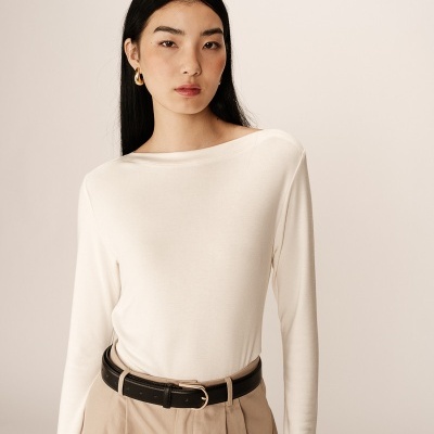 Mulher com camisola branca de manga comprida, calças bege e cinto preto
