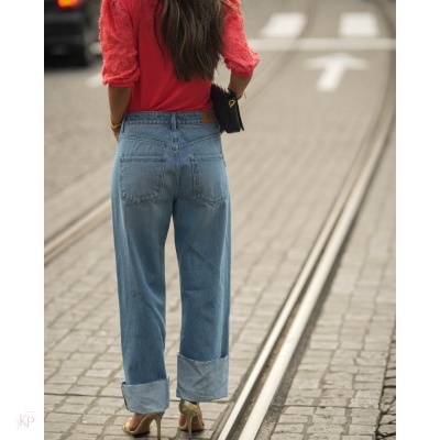 Calças de ganga azuis de cós alto com bainha dobrada vistas por trás numa rua com carris e pavimento de paralelepípedos