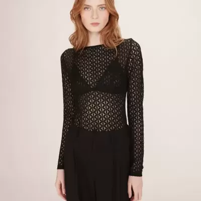 Blusa preta de renda com padrão geométrico e mangas compridas, vestida com calças pretas.