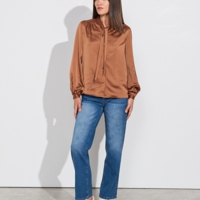 Mulher com blusa castanha de cetim, calças de ganga azuis e sapatilhas brancas em fundo branco