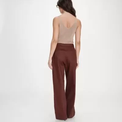 Mulher vista de costas com top bege sem mangas e calças castanhas largas