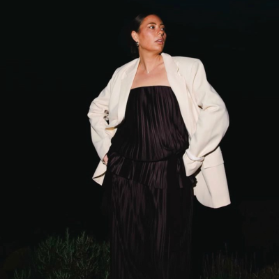 Pessoa com vestido preto plissado e casaco branco num ambiente noturno