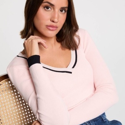 Mulher com camisola rosa clara de malha canelada com detalhes pretos sentada numa cadeira de madeira com assento em palhinha