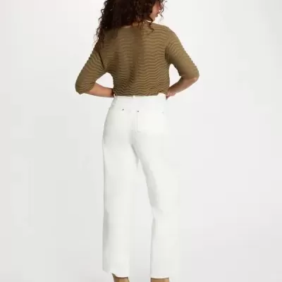 Mulher de costas com camisola castanha, calças brancas e botins camel.