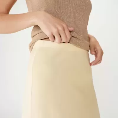 Pessoa vestindo top castanho claro brilhante e saia creme clara lisa