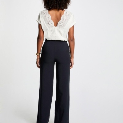 Mulher de costas a usar blusa branca com rendados e calças pretas largas