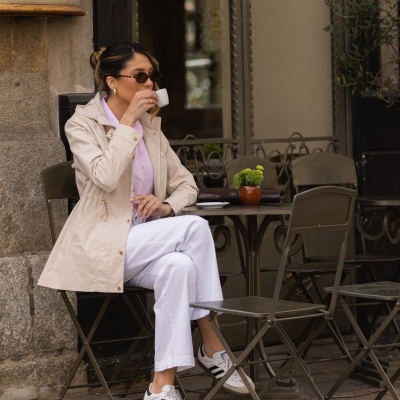 Mulher sentada numa esplanada a beber café com roupa casual.