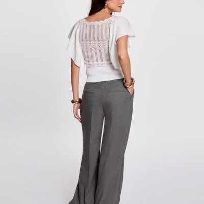 Mulher vestindo blusa branca rendada e calças cinzentas largas vista de costas