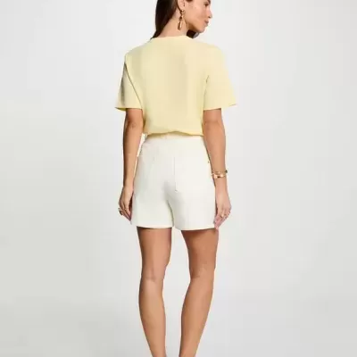 Mulher de costas com t-shirt amarela, calções brancos e sandálias brancas com tachas