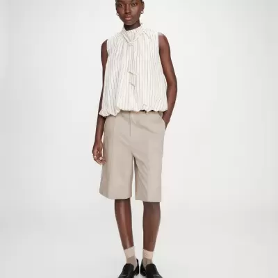 Mulher a usar blusa branca às riscas e calções bege em fundo branco