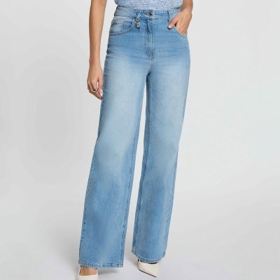 Calças de ganga azuis de corte largo com blusa azul clara e sapatos brancos de salto