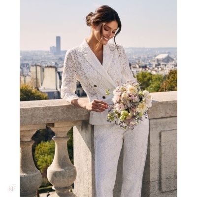 Mulher com fato branco de renda e ramo de flores numa varanda exterior.
