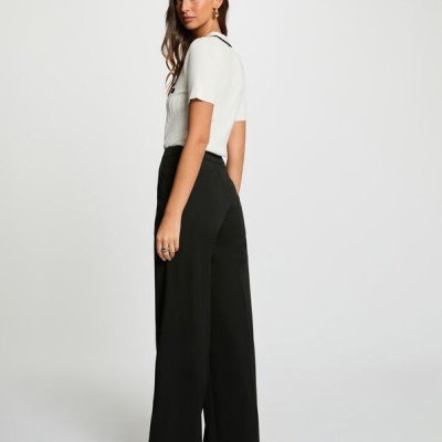 Mulher de costas com camisa branca de manga curta e calças pretas largas em fundo branco