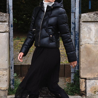 Mulher com casaco acolchoado preto e vestido preto num portão de ferro azul