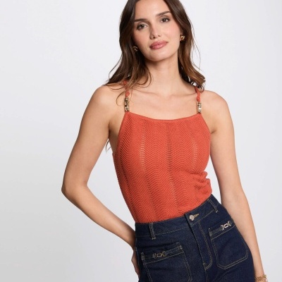 Top laranja de malha e calças jeans escuras num estúdio com fundo branco