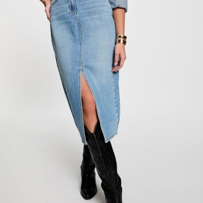 Saia midi de ganga azul clara com racha frontal, cinto preto, camisa de ganga e botas pretas até ao joelho.