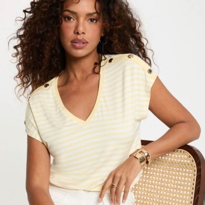 Top feminino amarelo claro com riscas brancas, botões nos ombros, e modelo sentada numa cadeira com encosto em palhinha.