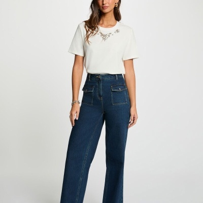 Mulher com t-shirt branca com padrão floral e calças de ganga azul escuro