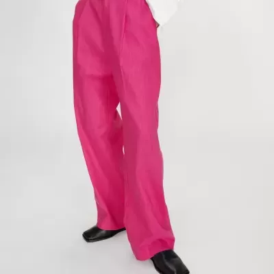 Calças largas rosa com botão castanho e sapatos pretos em fundo branco