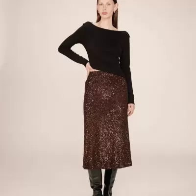 Mulher com blusa preta, saia castanha com lantejoulas e botas pretas