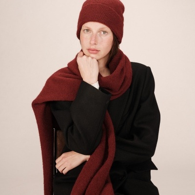 Mulher com gorro e cachecol de malha vermelho escuro e casaco preto sentada