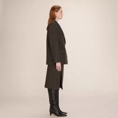 Mulher com blazer cinza escuro, saia com racha e botas pretas altas.