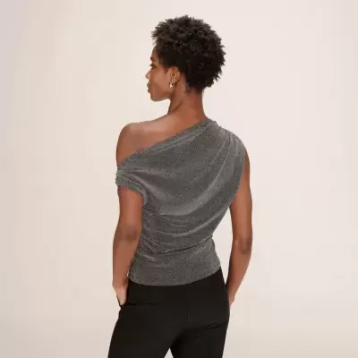 Mulher de costas usando blusa cinza brilhante com um ombro à mostra e calças pretas.