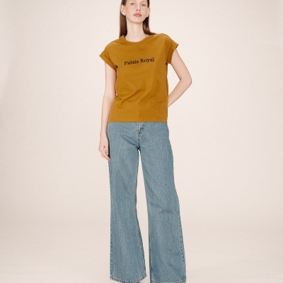 Mulher a usar t-shirt mostarda com texto e calças de ganga largas num fundo bege