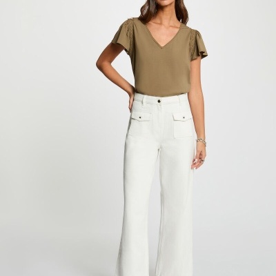 Mulher vestindo blusa verde caqui, calças brancas largas e botas castanhas