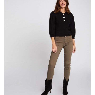 Mulher vestindo camisola preta com botões brancos e calças castanhas, botas pretas, em fundo cinzento claro