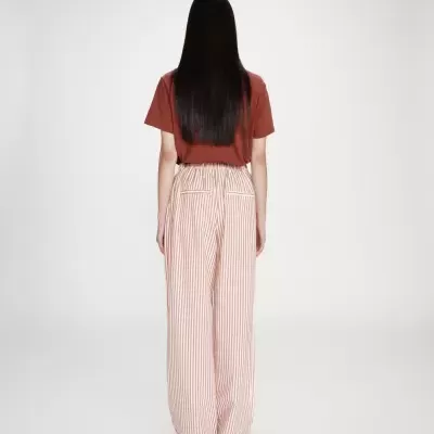 Pessoa de costas com t-shirt castanha e calças largas às riscas brancas e castanhas