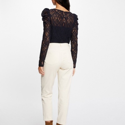 Mulher de costas com blusa de renda preta e calças brancas, botins castanhos