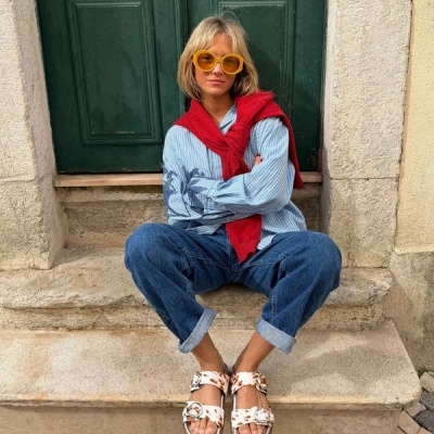 Mulher sentada em degraus de pedra com roupa casual e óculos amarelos grandes