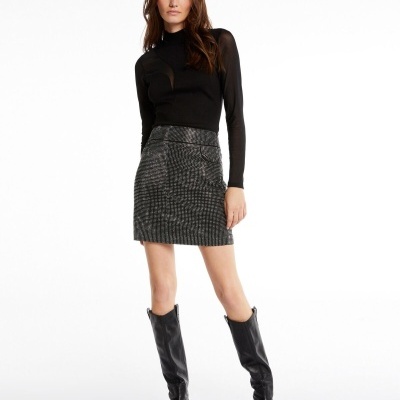 Mulher vestindo saia curta cinza com padrão pied-de-poule e camiseta preta com mangas compridas, usando botas pretas até ao joelho.